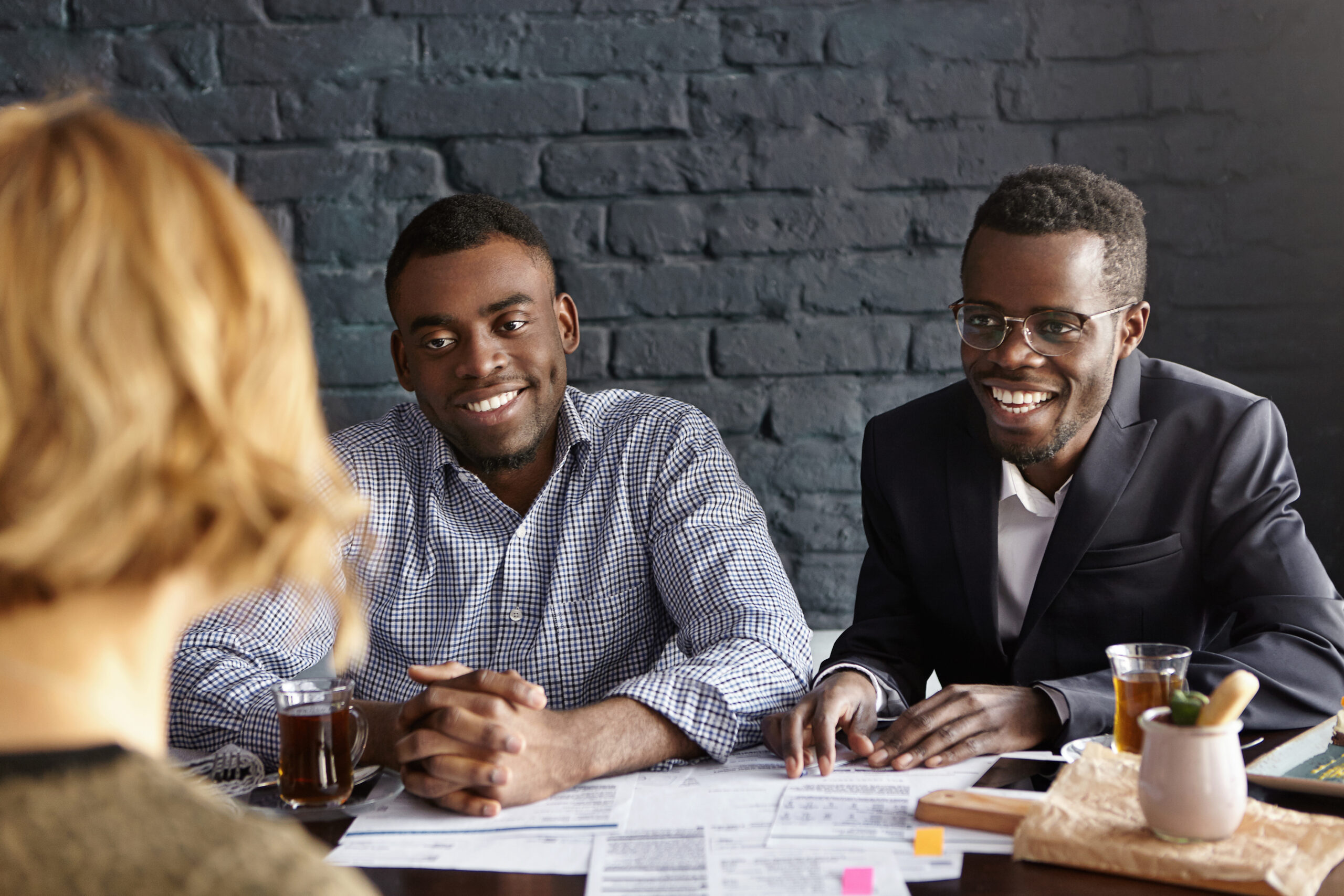 Unrecognizable female with shirt hairstyle is about to be hired for desired position in large company by two cheerful dark-skinned handsome recruiting experts, laughing happily during job interview